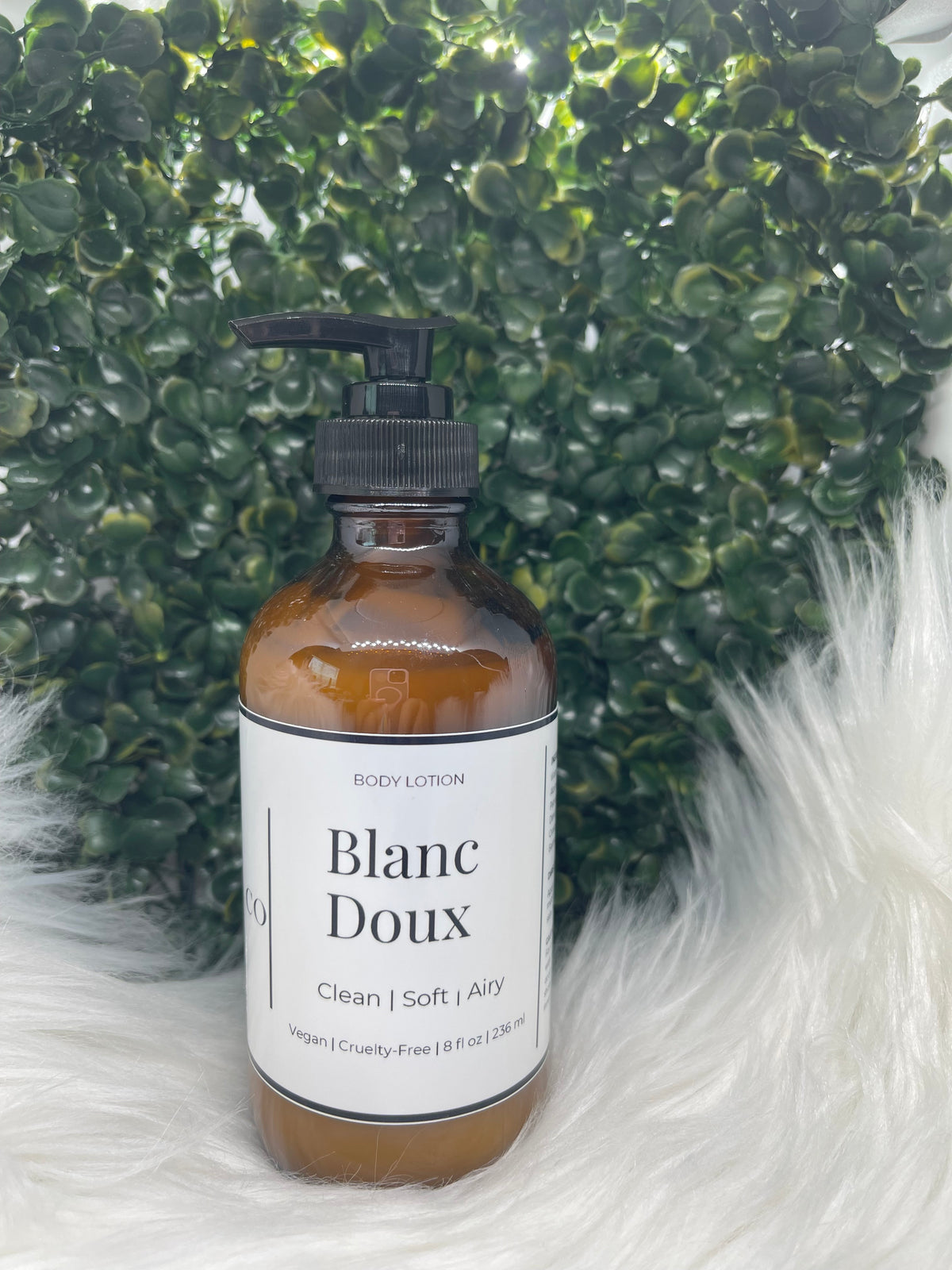 Bottle of Blanc Doux body lotion on a textured surface with green and white elements