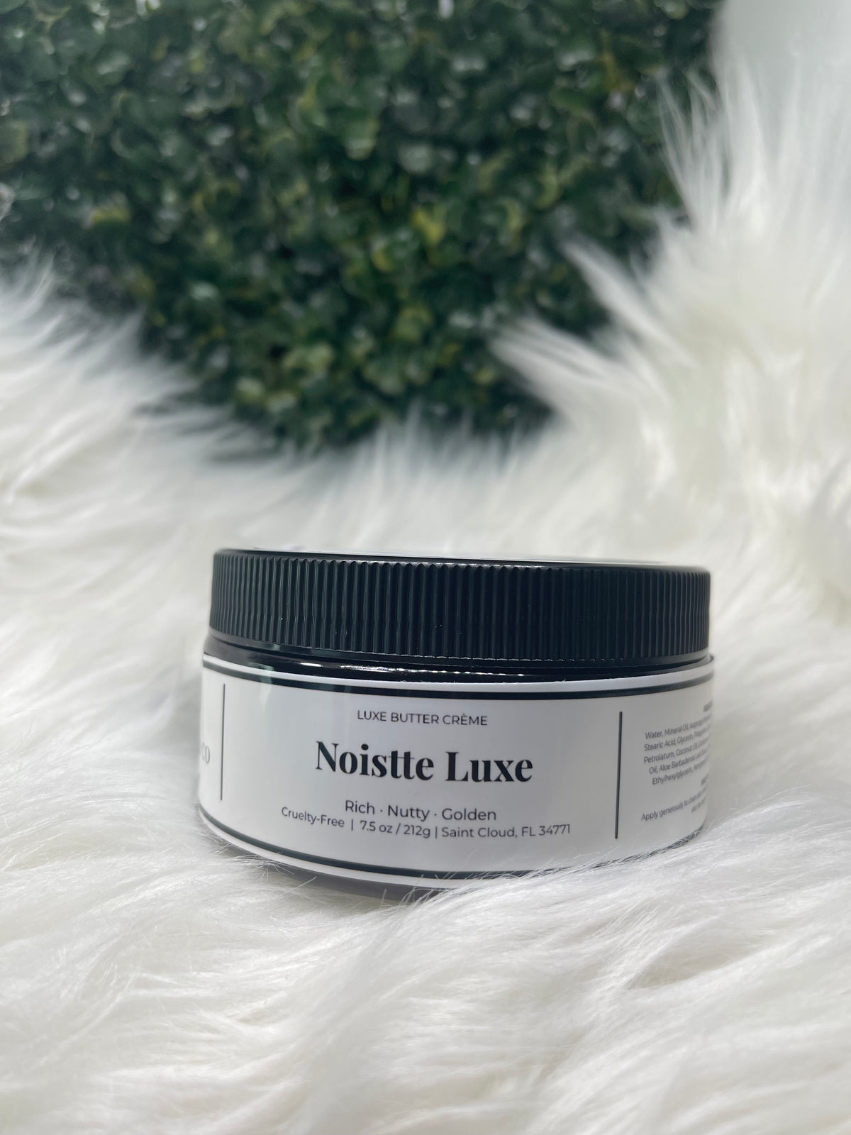 Jar of Noisette Luxe cream on a fluffy white surface with greenery in the background
