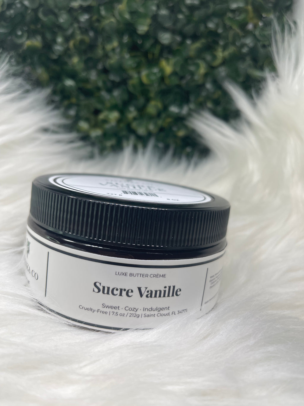 Jar of Sucre Vanille cream on a fluffy white surface with greenery in the background