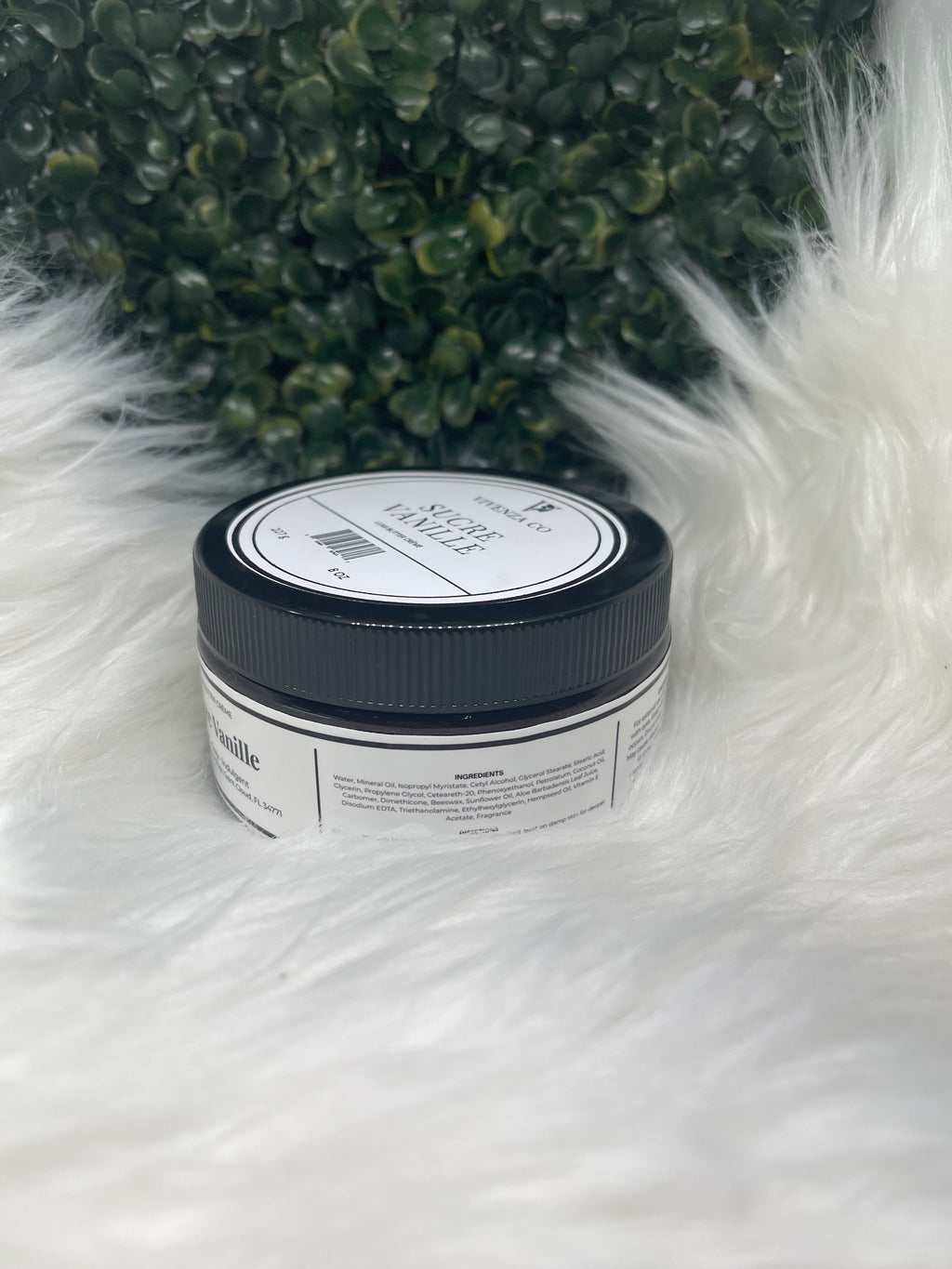 Jar of product on a fluffy white surface with greenery in the background