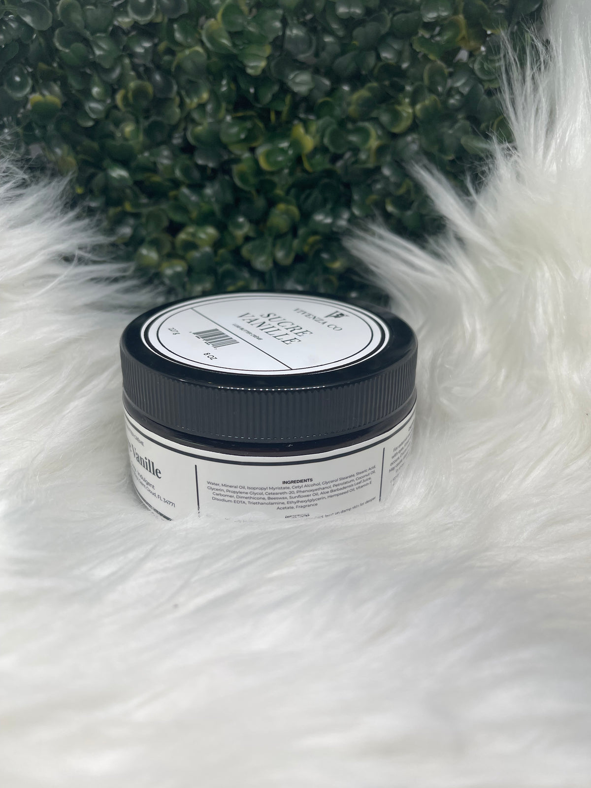 Jar of product on a fluffy white surface with greenery in the background