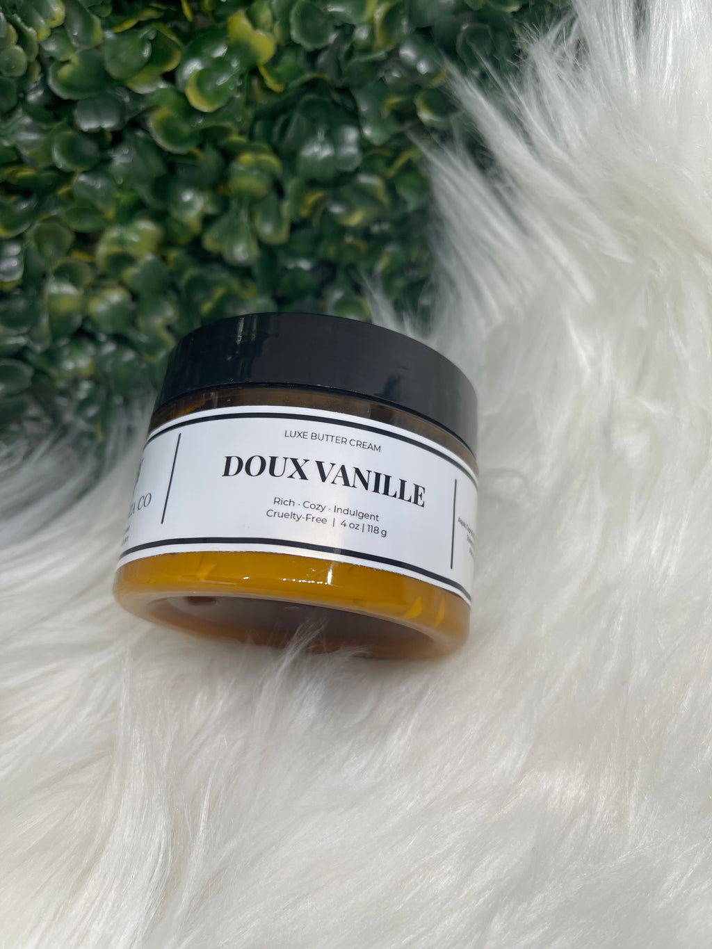 Jar of Doux Vanille on a fluffy white surface with green plants in the background