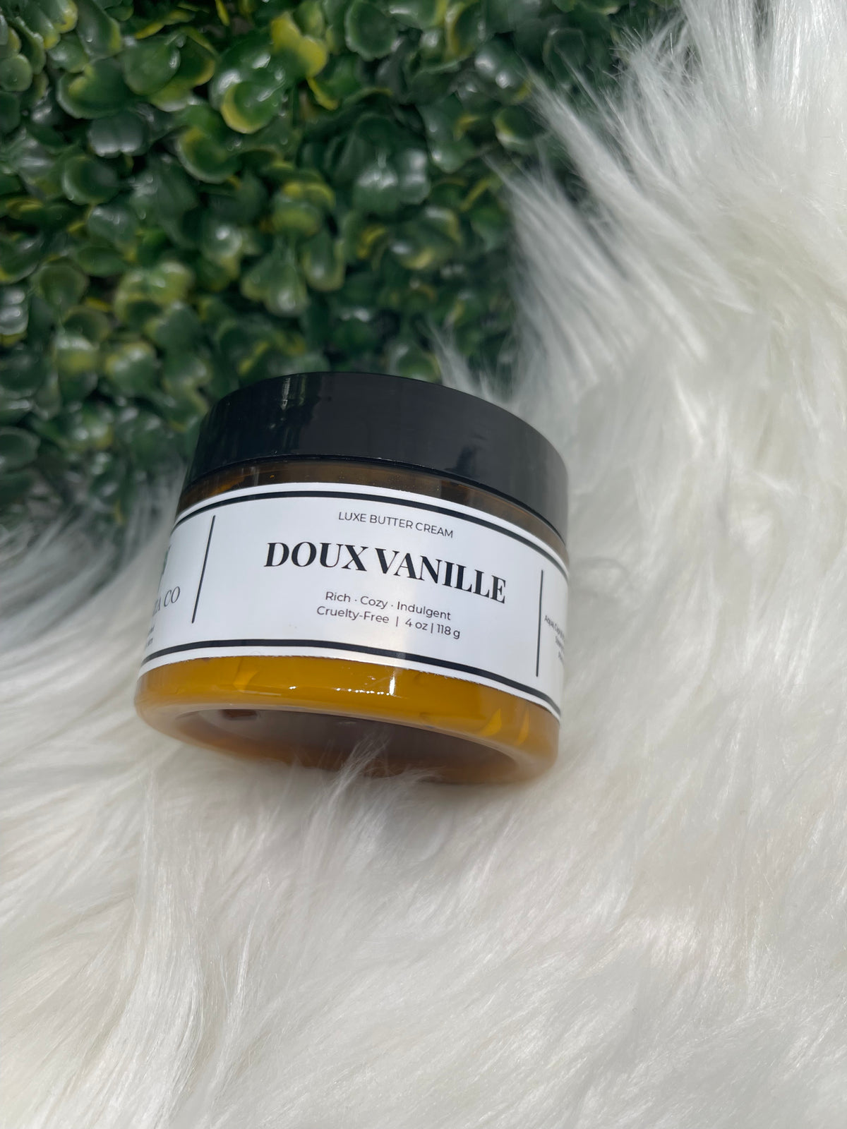 Jar of Doux Vanille on a fluffy white surface with green plants in the background