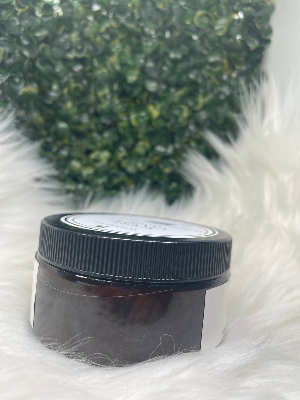 Small container with a black lid on a white fluffy surface next to green textured material