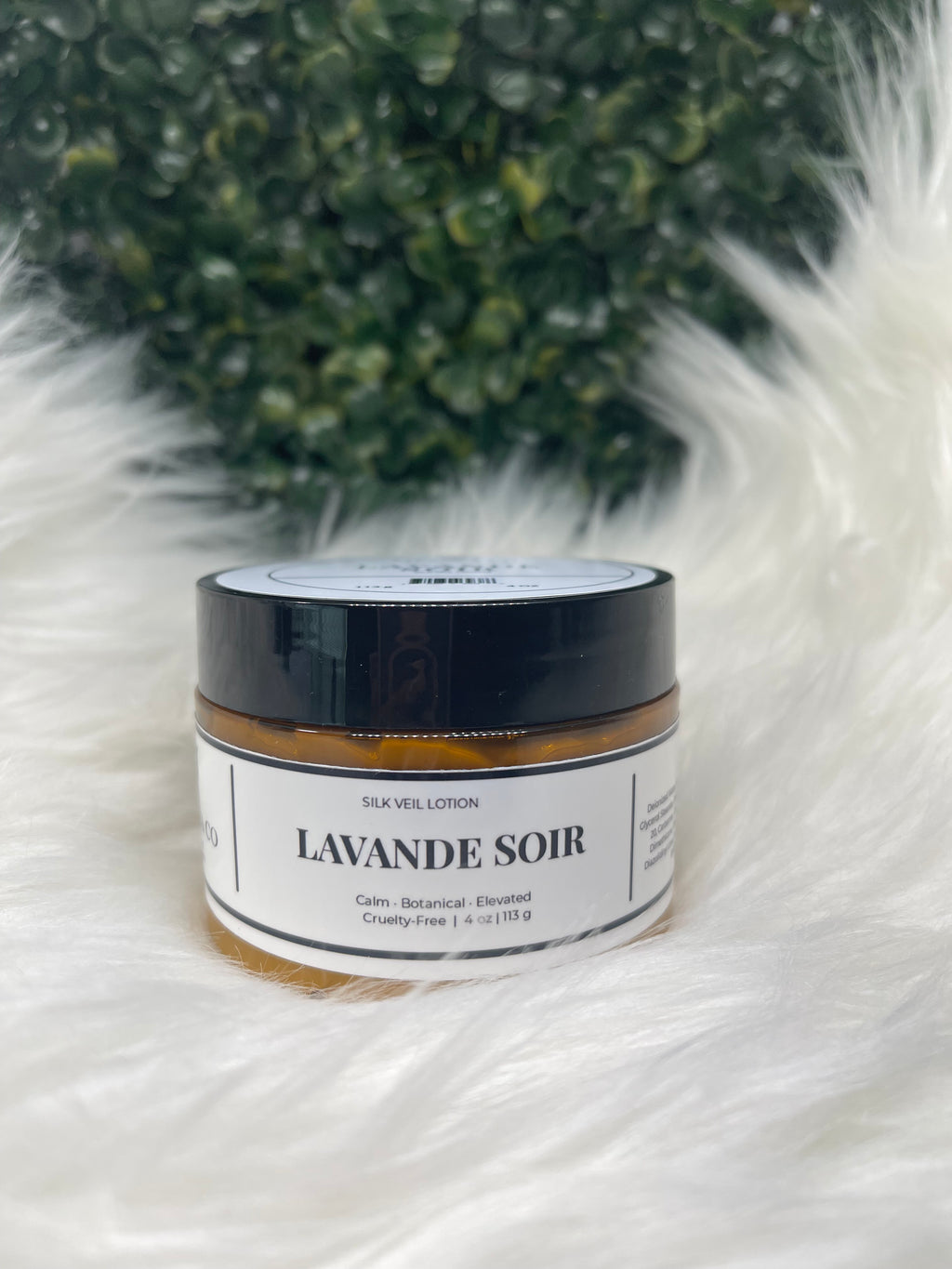 Jar of 'Lavande Soir' on a fluffy white surface with greenery in the background