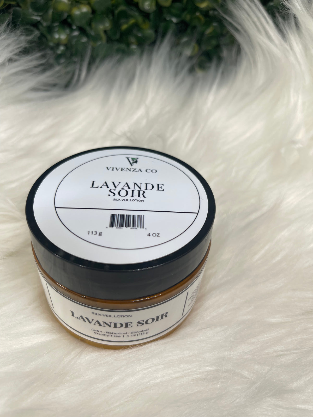 Jar of 'Lavande Soir' candle on a fluffy white surface with greenery in the corner.