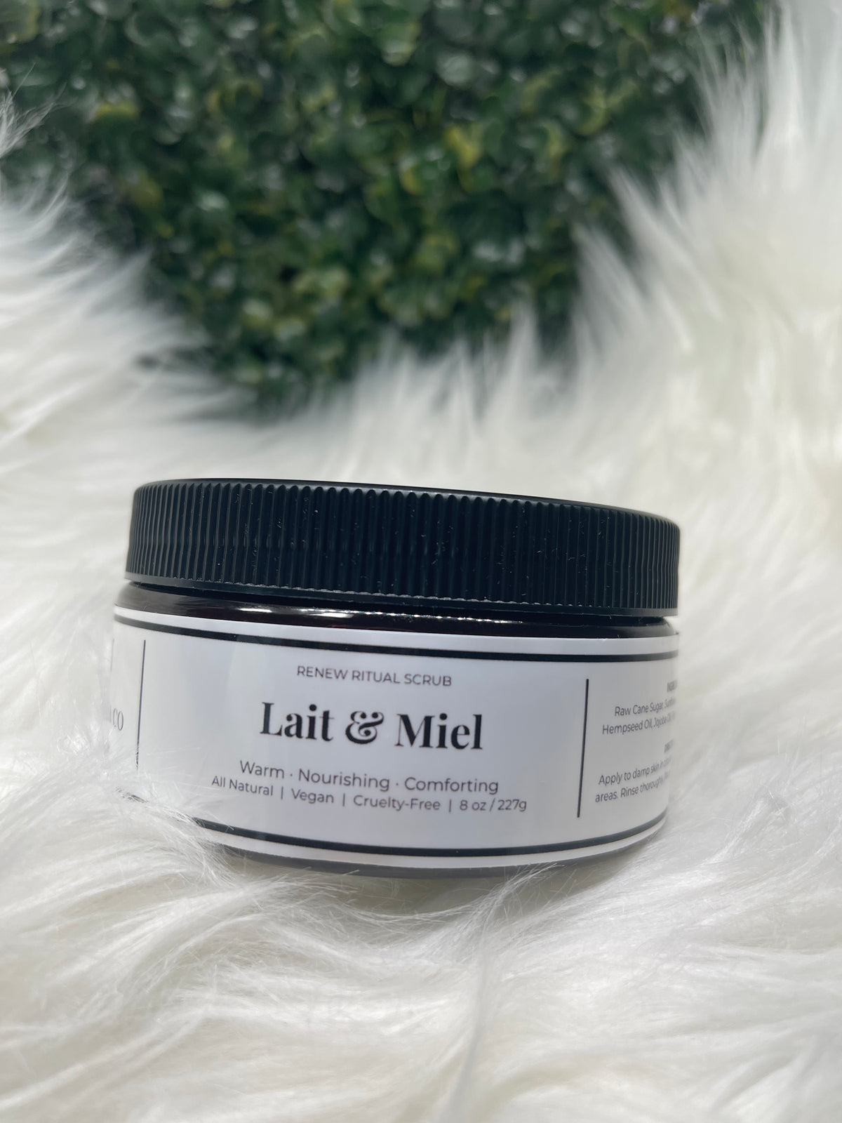 Jar of Lait & Miel product on a fluffy white surface with green leaves in the background