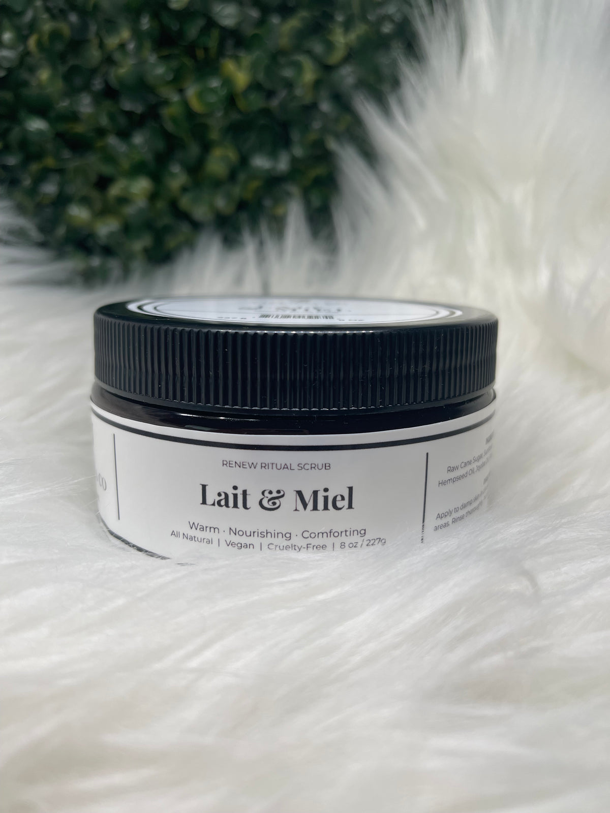 Jar of Lait & Miel cream on a fluffy white surface with greenery in the background