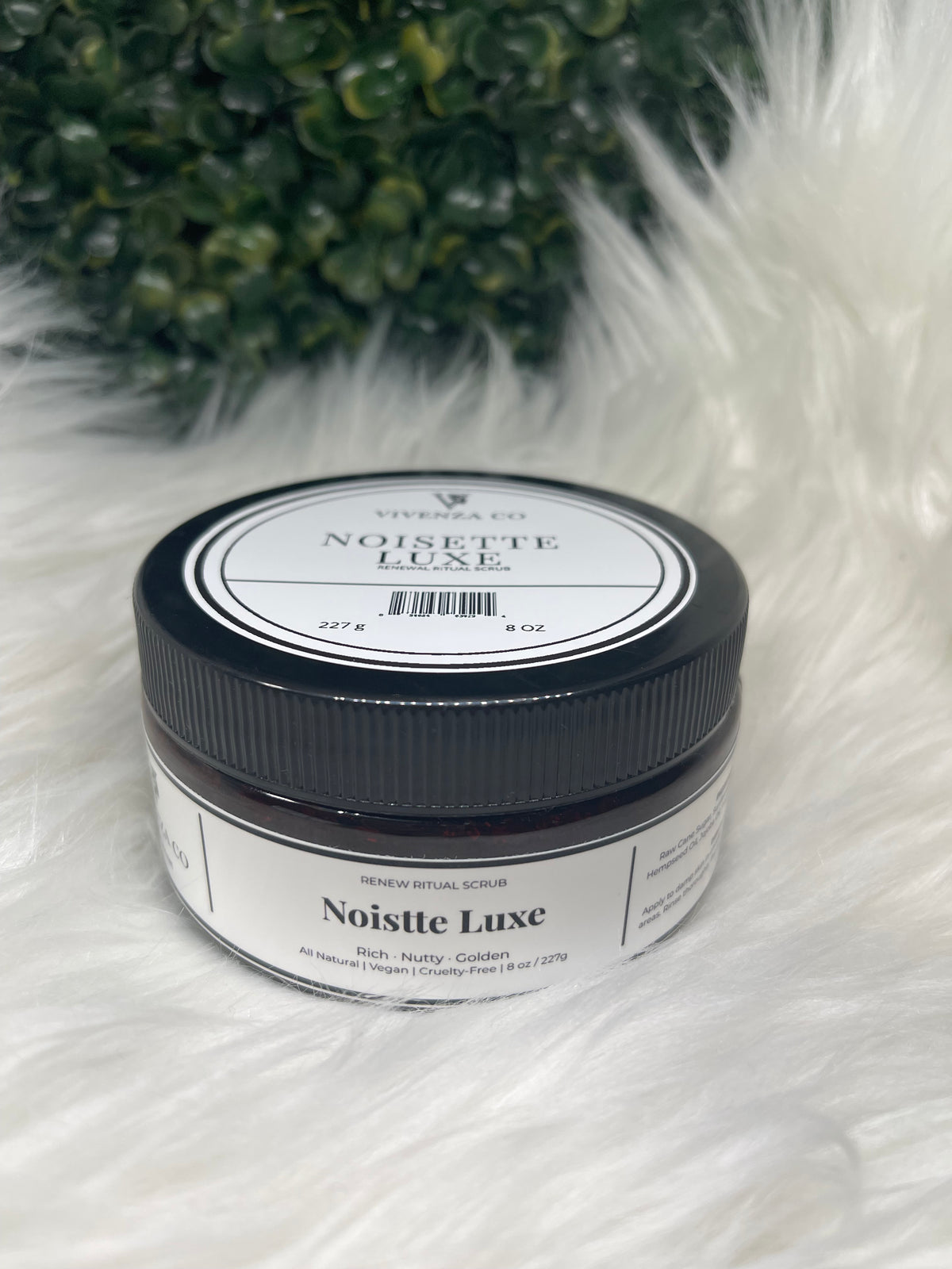 Jar of Noisette Luxe on a fluffy white surface with greenery